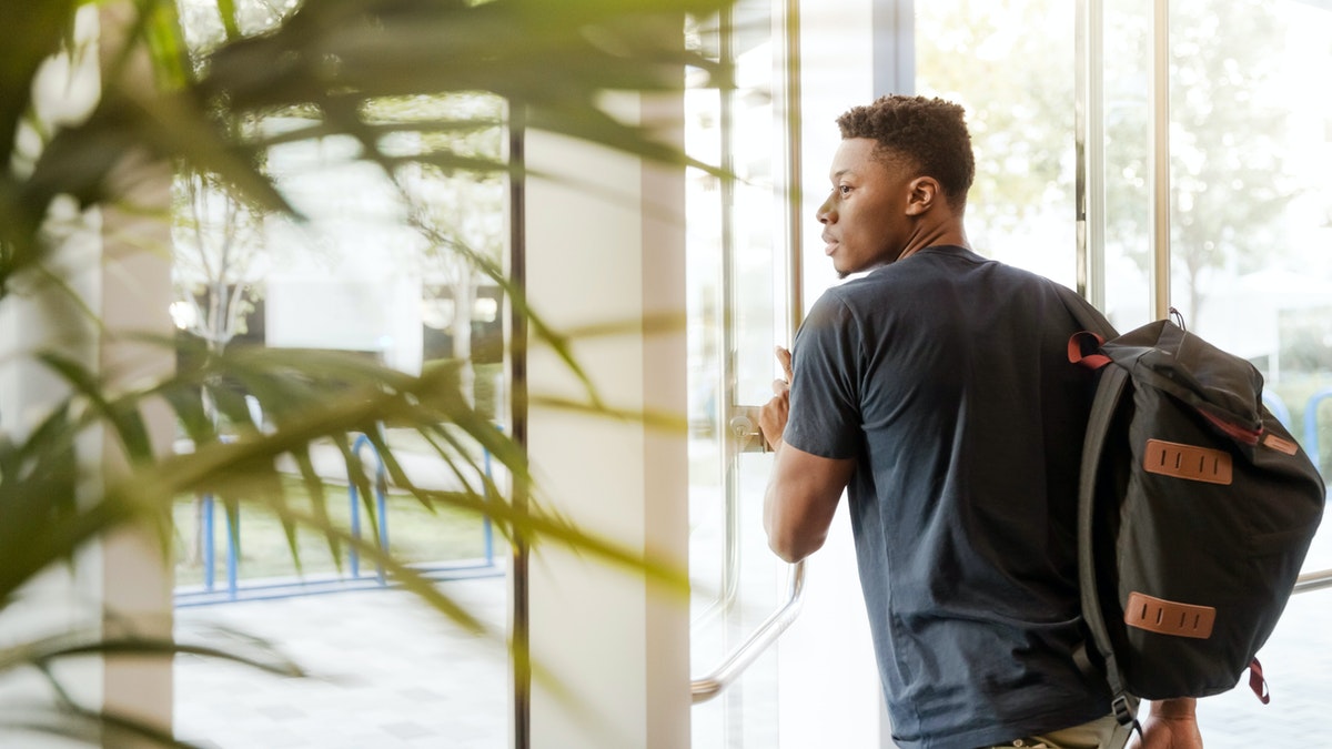 man looking outside window carrying backpack