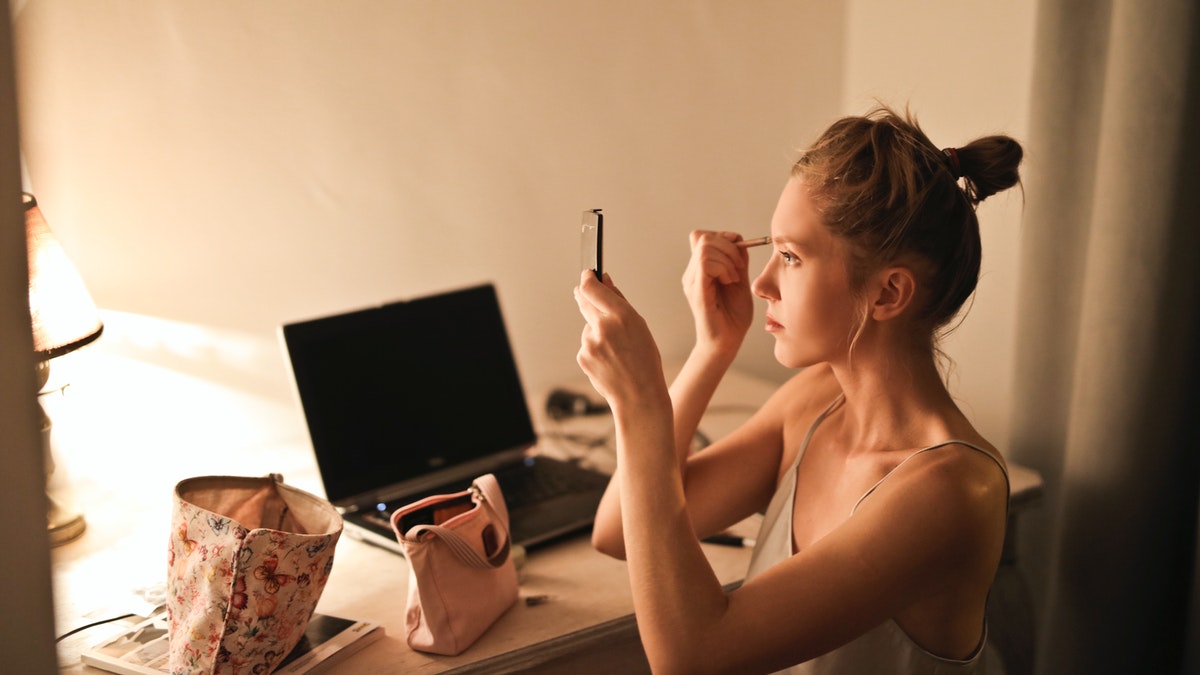 woman at desk with laptop doing her makeup