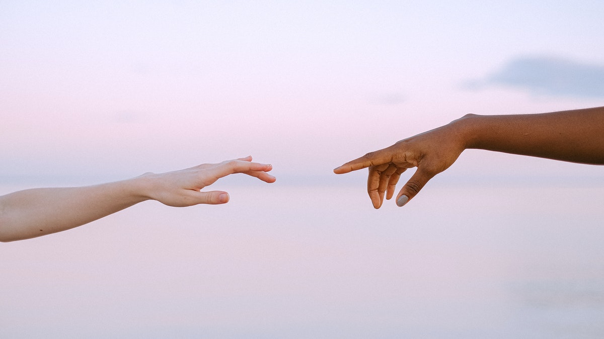 hands reach for each other against pink sky backdrop